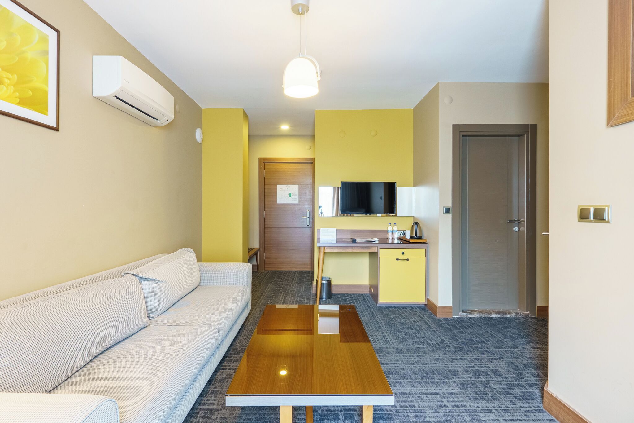Ein kompaktes Hotelzimmer mit einer Couch, einem Holztisch, einer Küchenzeile und einem Fernseher.