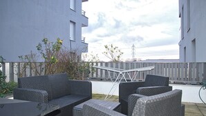 En utomhusplats med sittmöbler i rotting, ett metallbord och utsikt över en byggnad och himlen.