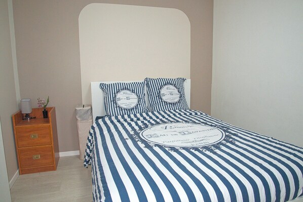 A bedroom with a bed featuring a striped bedspread and matching pillows, a wooden nightstand with a lamp, and a small vase with flowers.