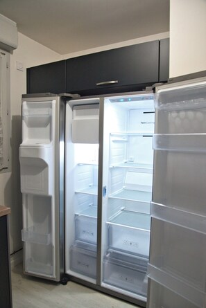 A kitchen with two refrigerators, a black cabinet, and a white wall.
