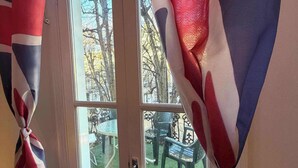Ikkuna, jossa on verhot sidottu rusetilla, ovi sekä näkymä ulkokalusteisiin ja puihin.