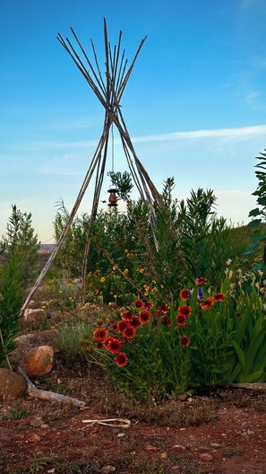 Un jardin agrémenté d’une structure en bois, peut-être un tipi, entouré de différentes plantes et fleurs.