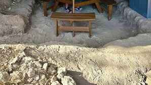 Una persona sentada a una mesa de madera con un centro de piedra, bajo una estructura que parece una cueva.