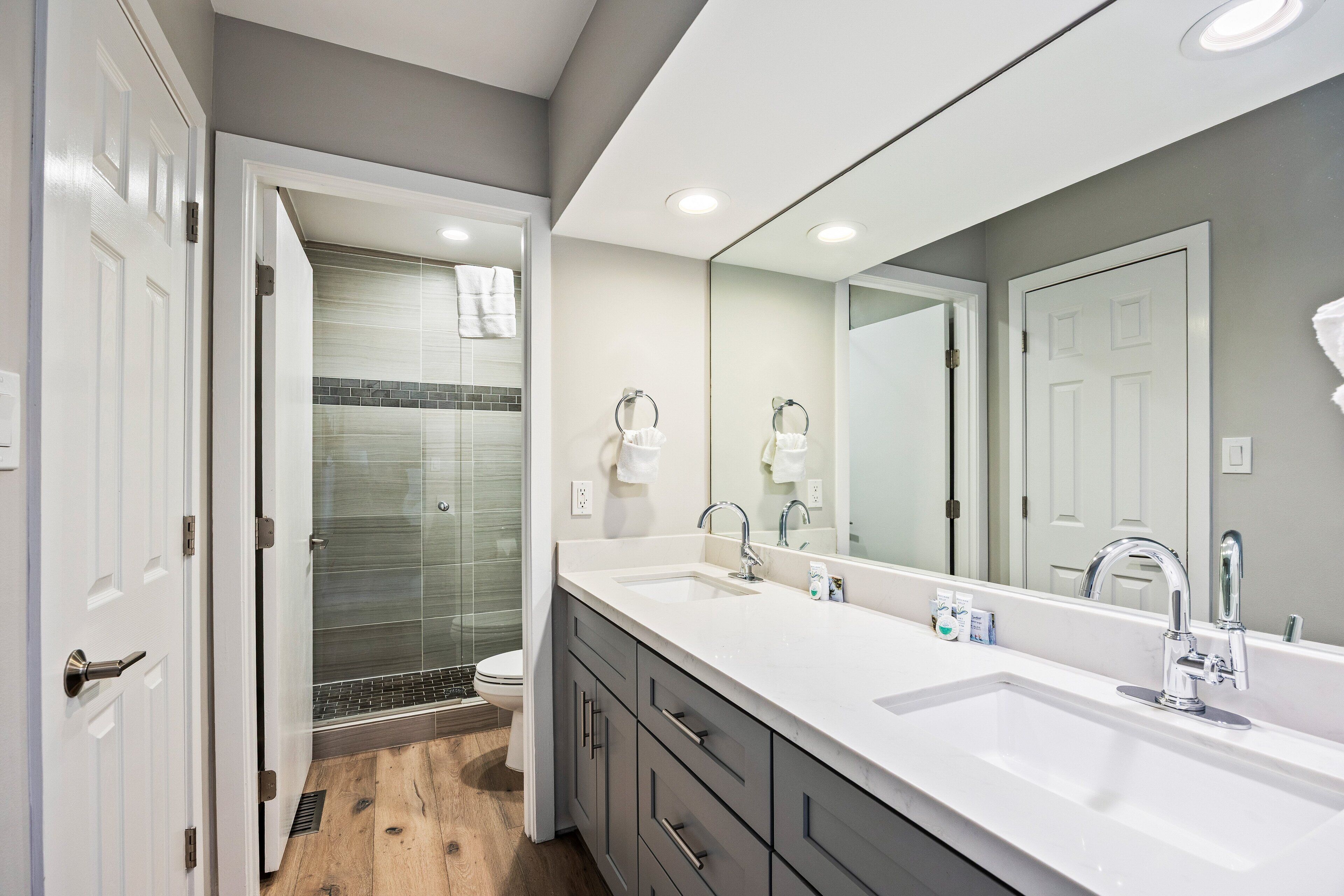 A modern bathroom with a large mirror, two sinks, and a shower.