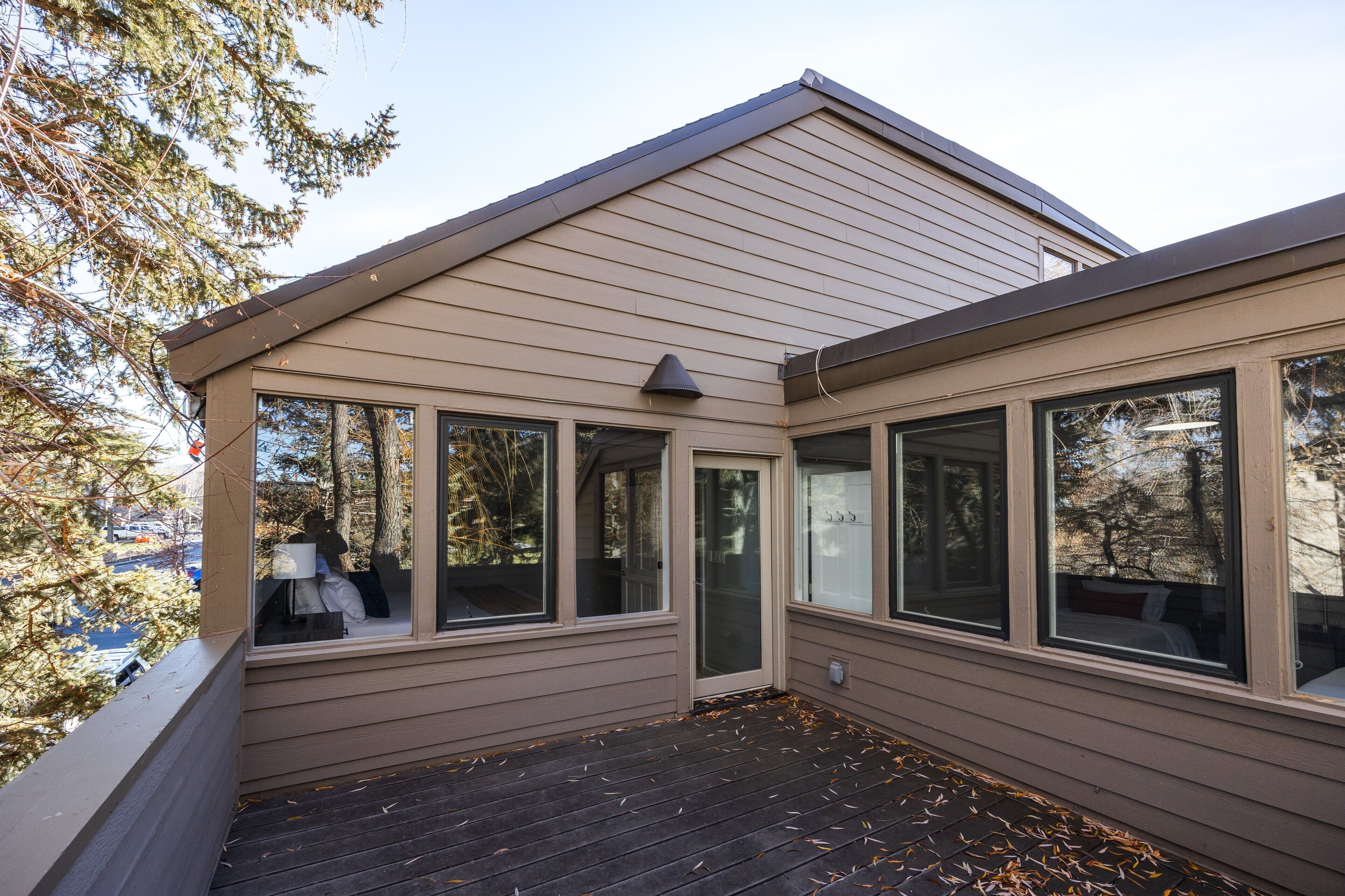 A covered deck with a view of a residential area, large windows, and a door.