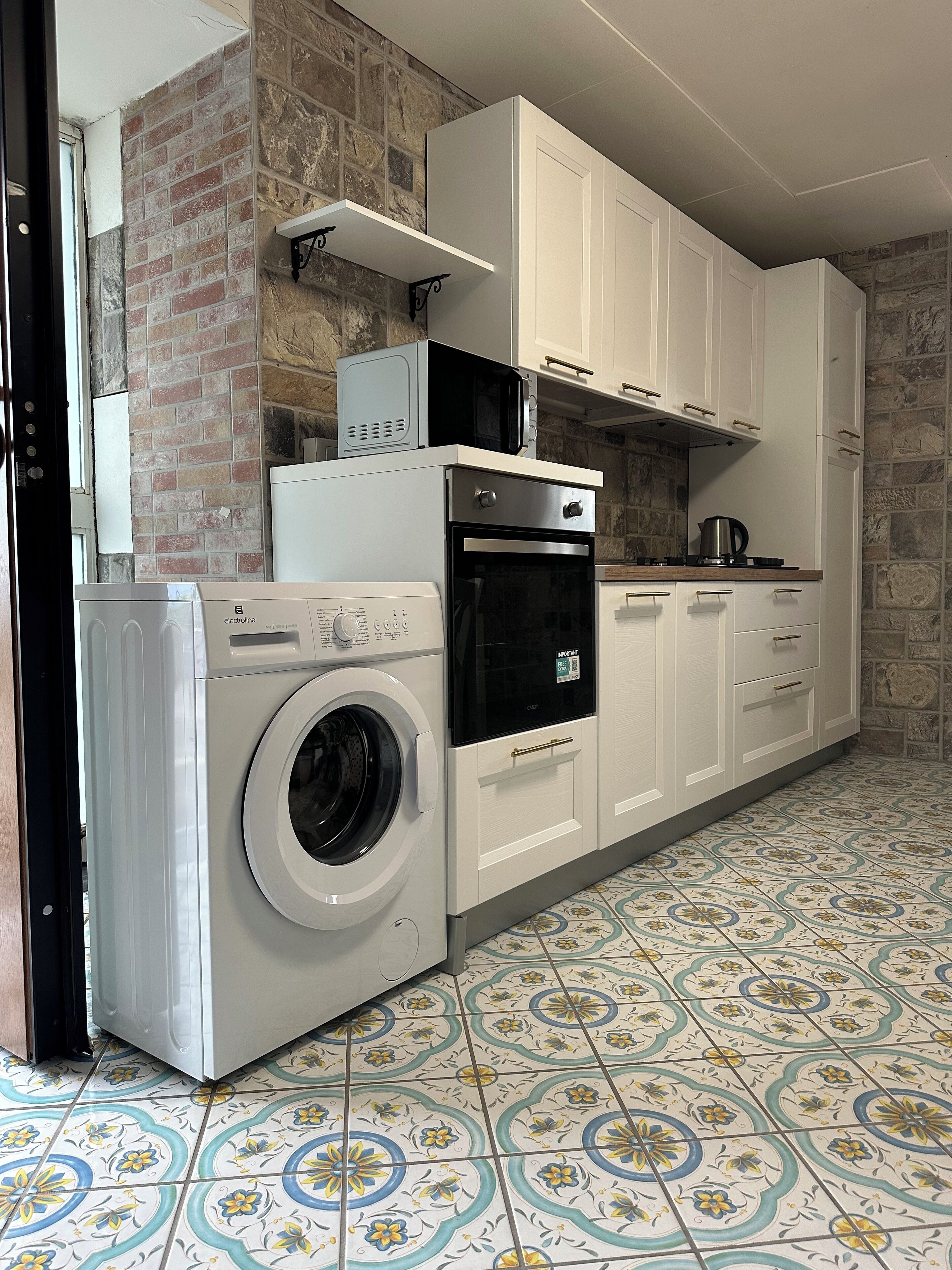 A compact kitchen with a washing machine, microwave, oven, and a coffee maker on the countertop.