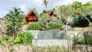 Un resort con cabañas de madera, abundante vegetación y un muro de contención de piedra.