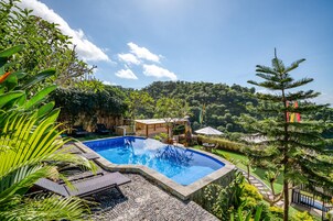 Una piscina rodeada de plantas tropicales y vistas a una colina boscosa.
