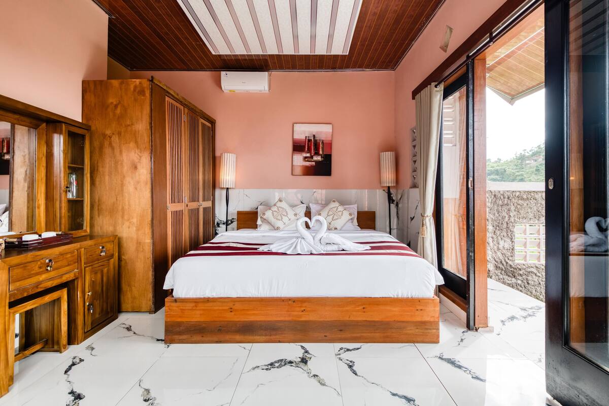 A bedroom with a wooden bed, a marble floor, a wooden wardrobe, and a large window with a view.