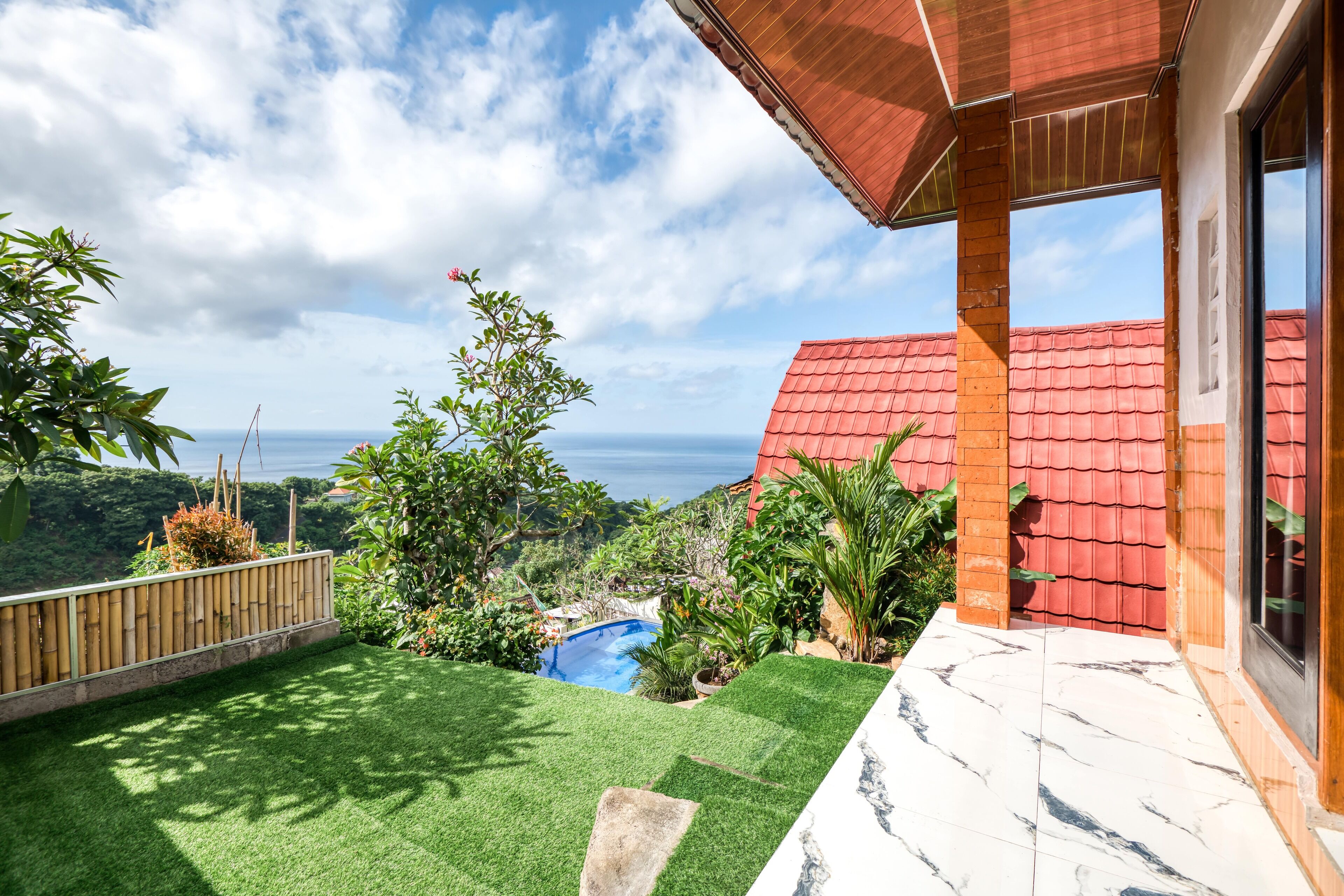 Un patio trasero con piscina, abundante vegetación y vista al océano.