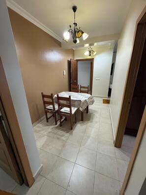 A dining area with a table set for four, surrounded by wooden chairs. A chandelier hangs from the ceiling, and the walls are painted in a warm beige tone. - 2-bedroom apartment in front of Tangier Stadium nearest stadium residence (Tanger)