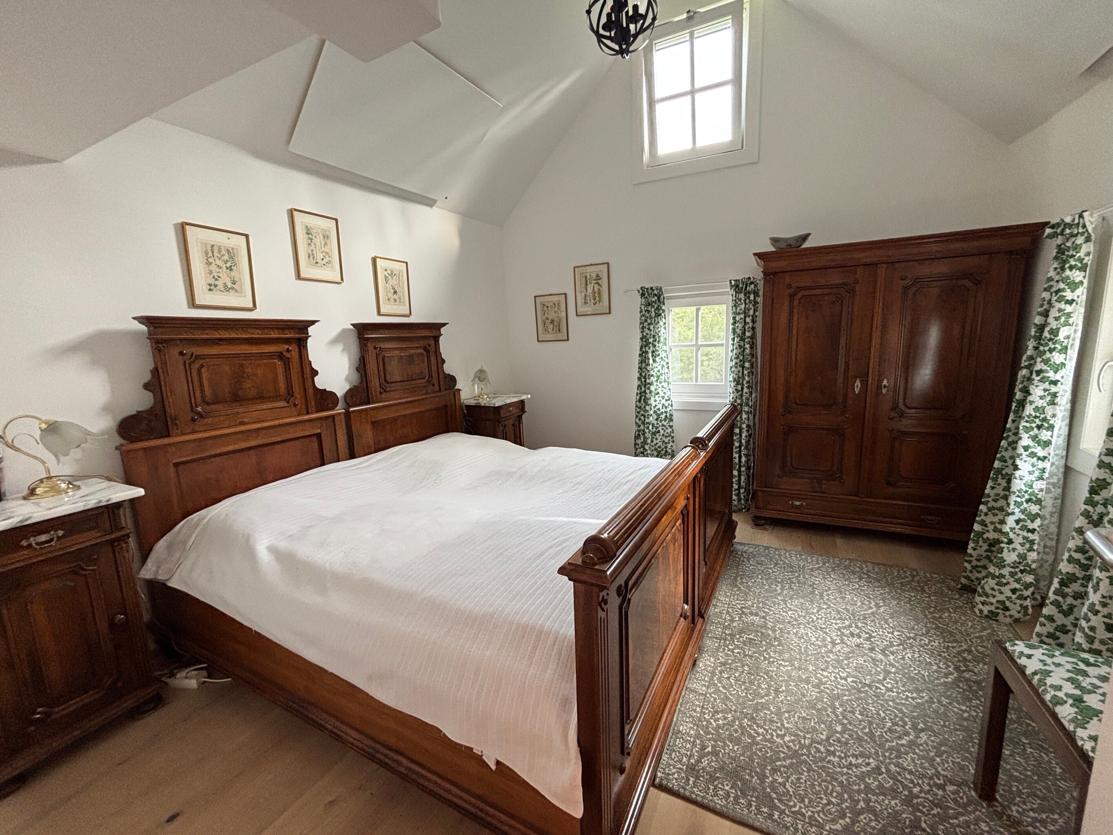 A bedroom with a large bed, wooden wardrobe, and a window with curtains.