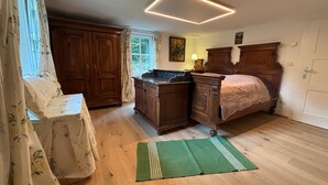Ein Schlafzimmer mit einem hölzernen Bett, einem Schminktisch, einem Fenster mit Vorhängen und einem grünen Teppich.