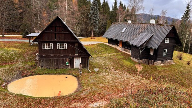Eine rustikale Holzhütte mit geneigtem Dach, einer Holzterrasse und einem kleinen Teich im Vordergrund.