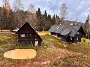 A rustic cabin with a sloped roof, a wooden porch, and a small pond in the foreground. - Holiday Home 'Lorenzfranzl' with Private Garden and Wi-Fi (Sankt Oswald ob Eibiswald)