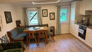 Ein Essbereich mit Holztisch und Stühlen, einer Couch und einer Küche mit weißen Schränken und Geräten.