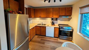A compact kitchen with wooden cabinets, a stainless steel refrigerator, a dishwasher, and a built-in oven. - Unit 33 - 4 bedrooms - 10 people (Beaupré)