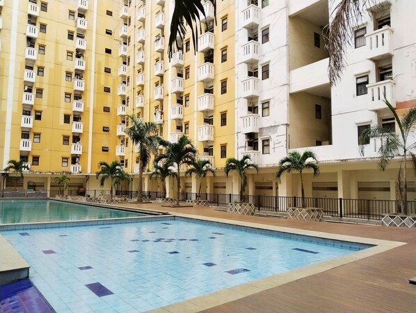A swimming pool surrounded by multi-story residential buildings with balconies. - Room 88 Kemang View Apartment (Bekasi)