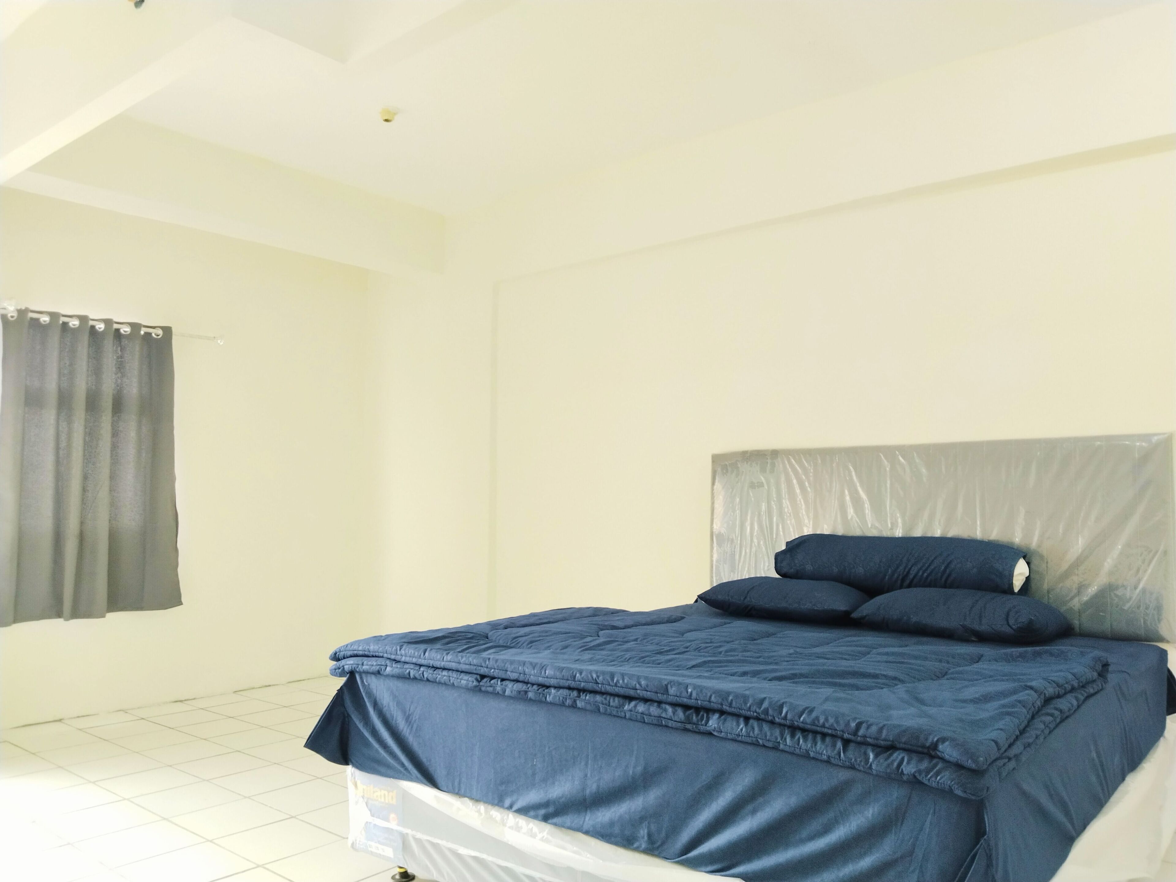 A bedroom with a bed covered in blue bedding, a grey curtain, and a white tiled floor.