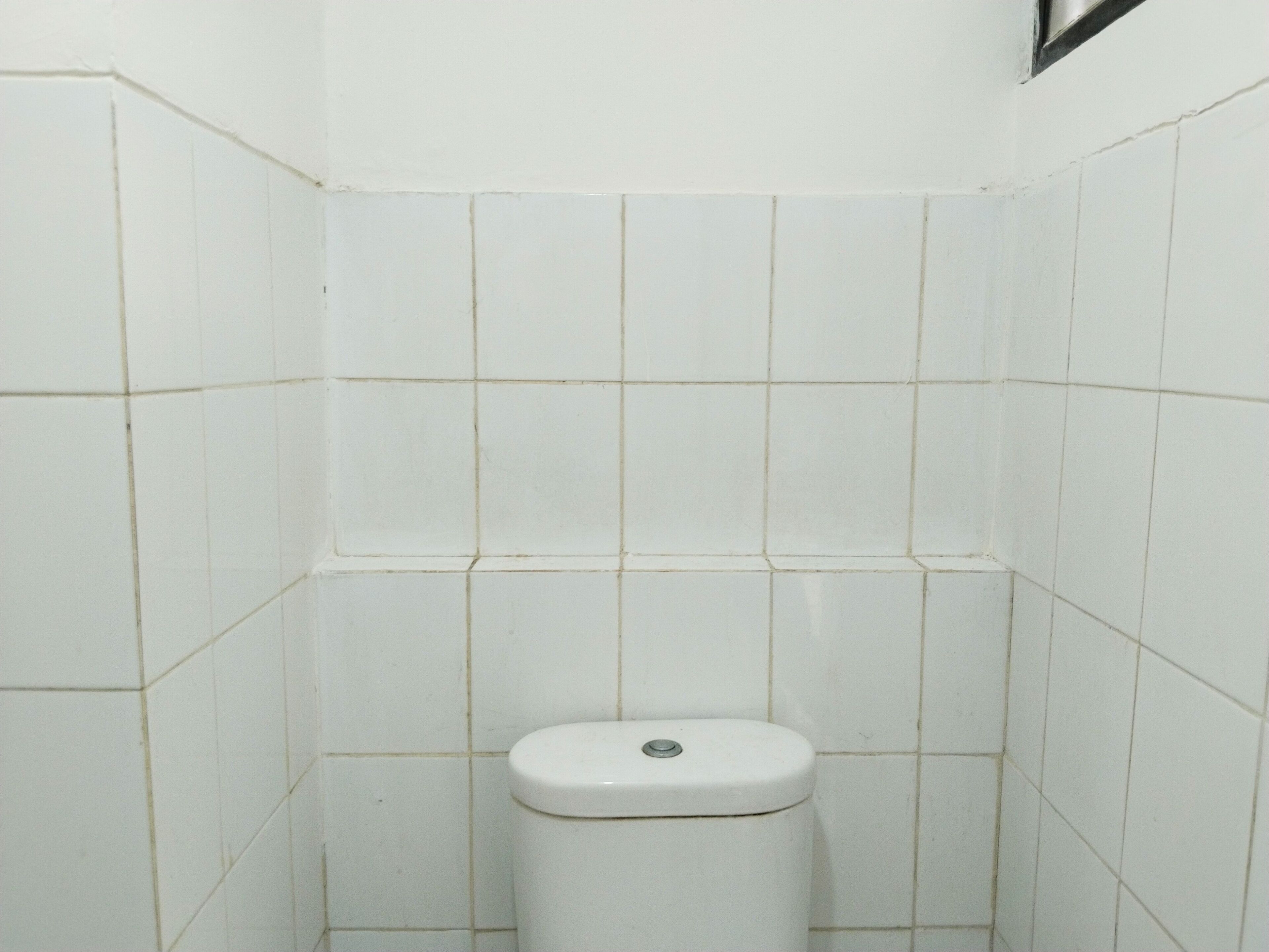 A small, white-tiled bathroom with a toilet.