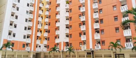 A multi-story residential building with balconies, a swimming pool, and palm trees.