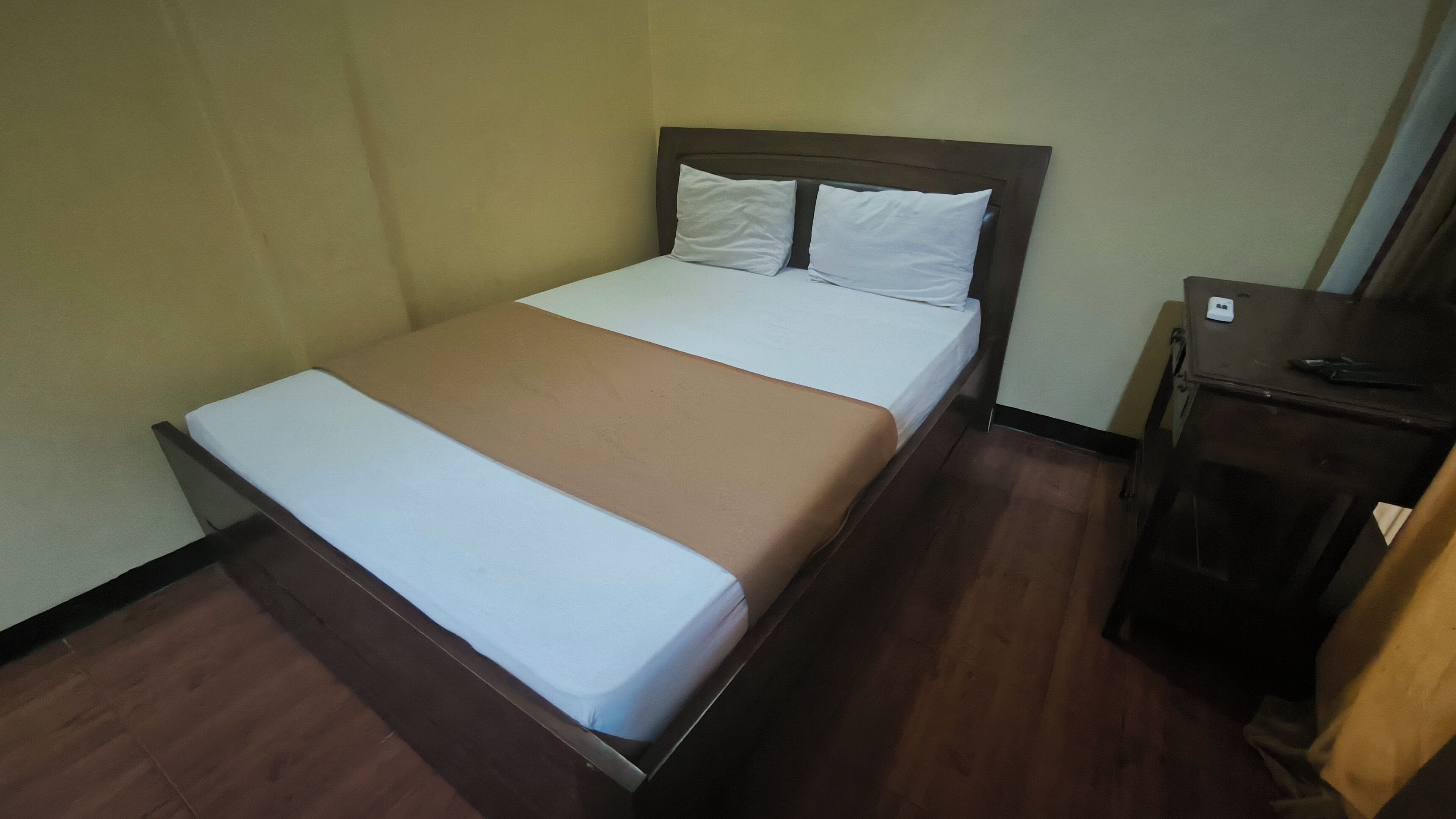 A single bed with a wooden frame, white bedding, and a brown blanket.
