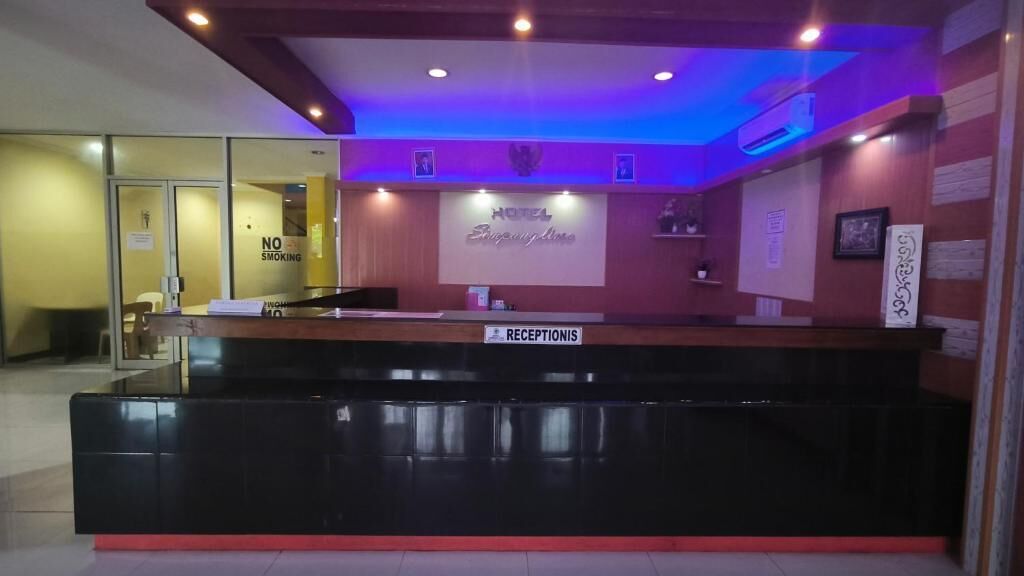 A hotel reception area with a reception desk, a 'No Smoking' sign, and a 'Receptionis' sign.
