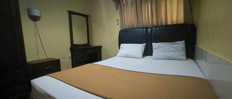 A hotel room with a bed, a dresser, a mirror, and a wall-mounted light fixture.