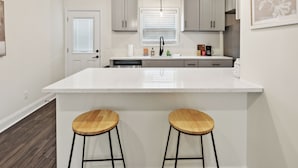 A modern kitchen with a large island, two bar stools, and pendant lighting. - Alto O4 I Modern New Construction 2Bd Apartment (Clarksville)