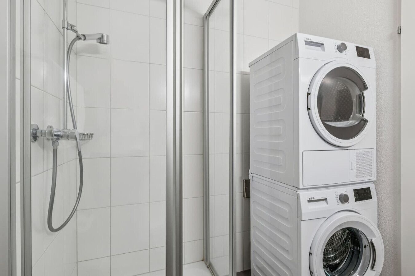 A compact bathroom with a shower, a stacked washer and dryer unit, and a tiled wall.