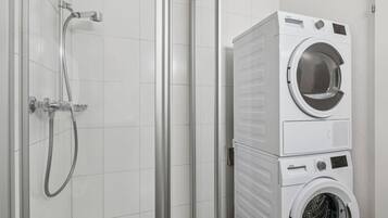 A compact bathroom with a shower, a stacked washer and dryer unit, and a tiled wall.