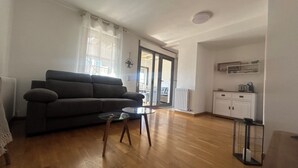 Un salon comprenant un canapé, une table basse et un coin cuisine avec des placards et un radiateur.