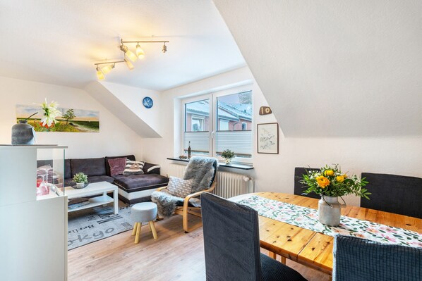 Un salon moderne comprenant un canapé, un fauteuil, une table à manger et une vue sur l’extérieur par une fenêtre.