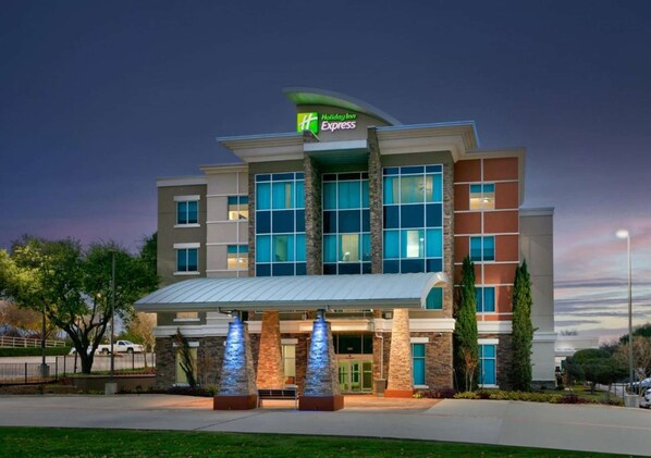 A Holiday Inn Express hotel with a modern design, featuring large windows and a prominent entrance. - Standard 2 Queen Room w/ Fridge | Pool. Gym. Wi-Fi (Dallas)