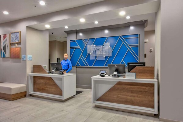A reception area with two desks, each equipped with a computer and a phone. There are framed artworks on the wall and a blue geometric wall design behind the desks. - Standard 2 Queen Room w/ Fridge | Pool. Gym. Wi-Fi (Dallas)