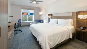 Habitación de hotel con cama, escritorio, silla, ventilador de techo y ventana con vista a árboles.