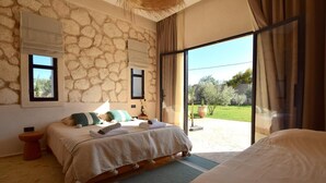 Un dormitorio con pared de piedra, una cama grande, una mesita de noche pequeña y vistas al exterior.