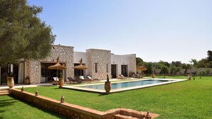 Un área junto a la piscina con un edificio de piedra, mobiliario exterior y un césped bien cuidado.