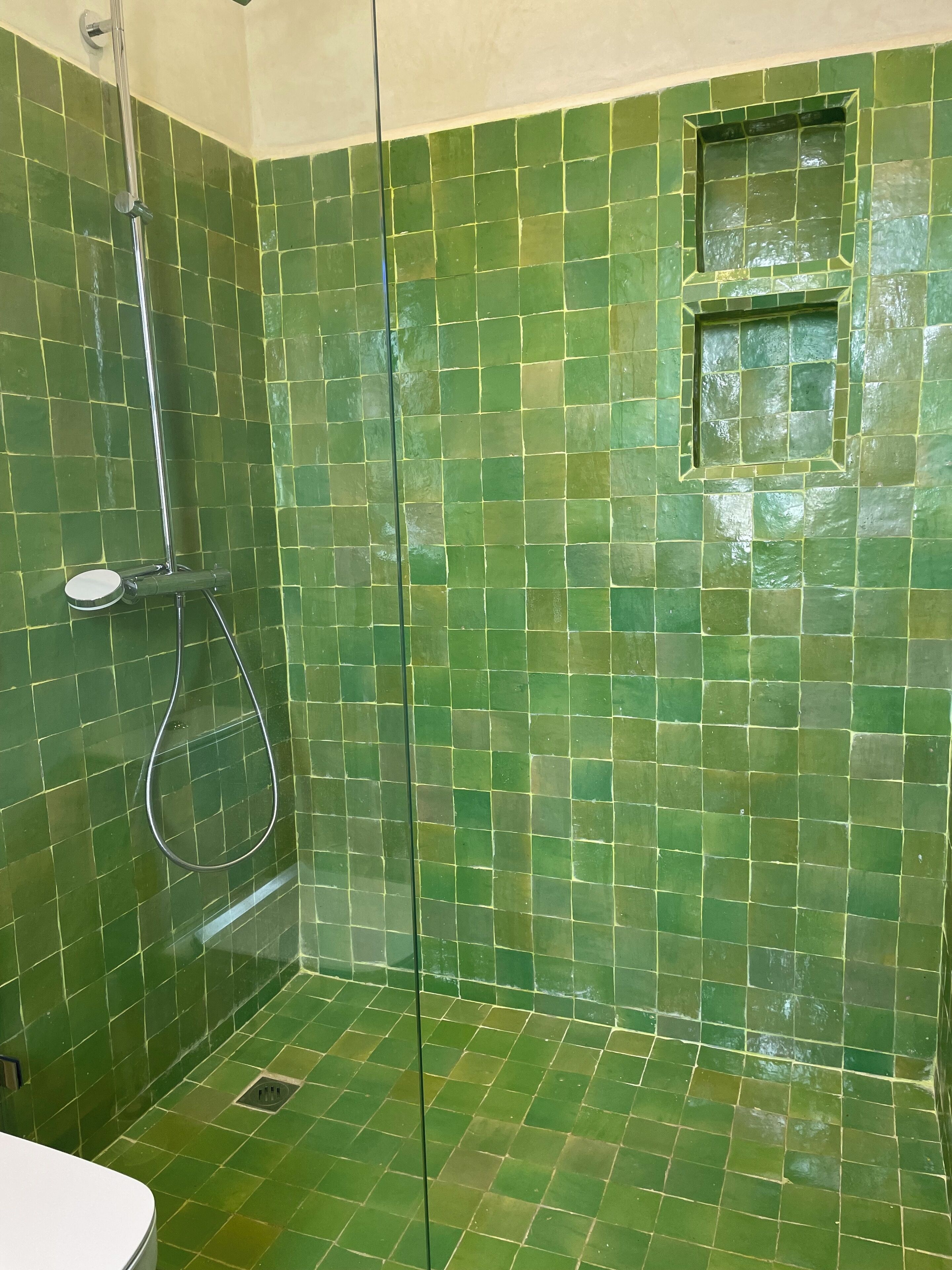 Une douche aux murs recouverts de carreaux de mosaïque verts, une douchette à main et une petite fenêtre.
