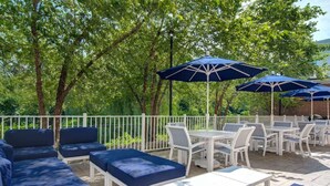 An outdoor patio with white furniture and blue cushions, surrounded by trees and covered by blue umbrellas. - Near Ridge Hill shopping. Breakfast. Pool. Bar. (Yonkers)