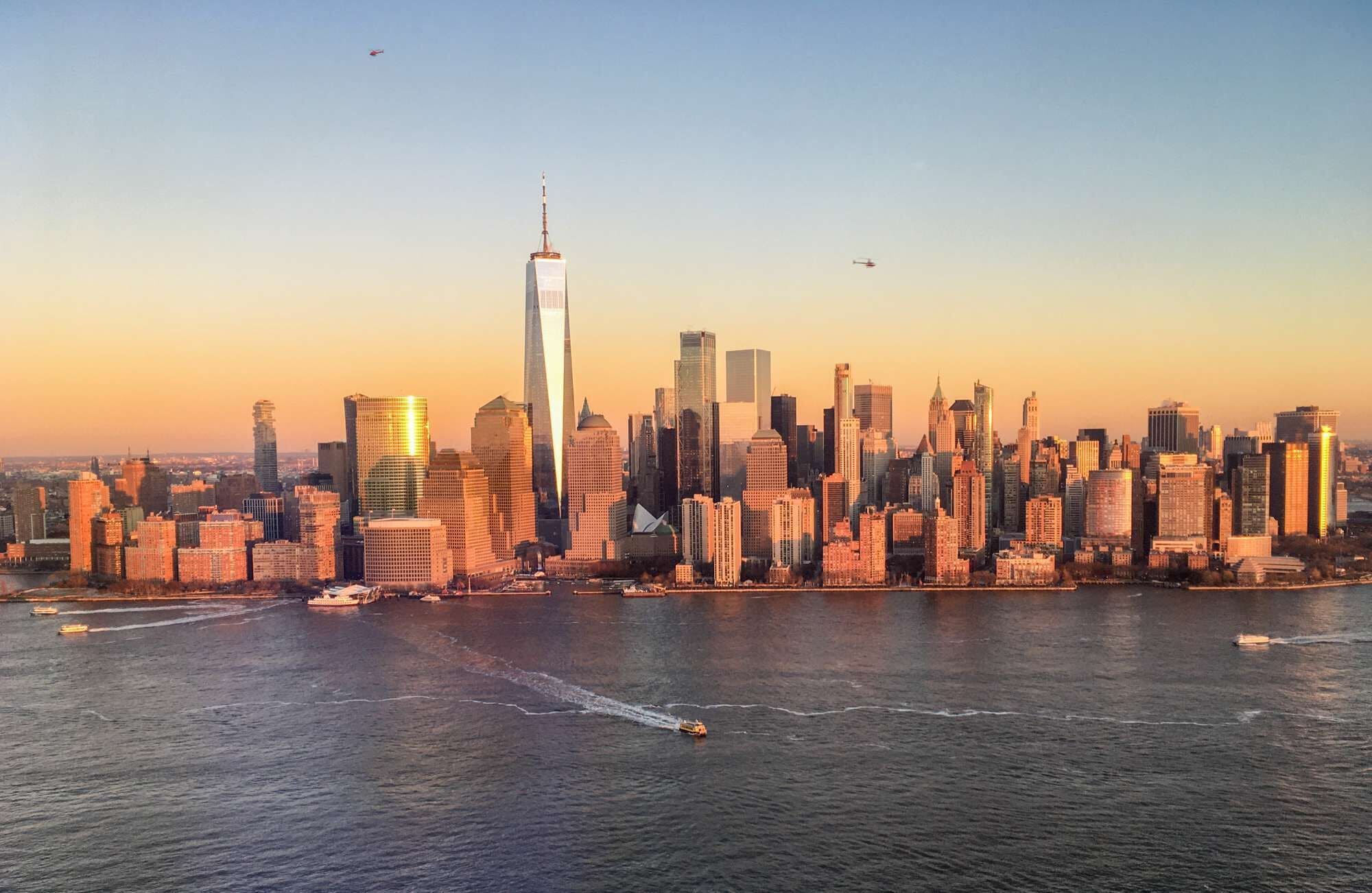 Une vue sur les toits d’une ville, avec un gratte-ciel imposant, une rivière où naviguent des bateaux et un ciel dégagé.