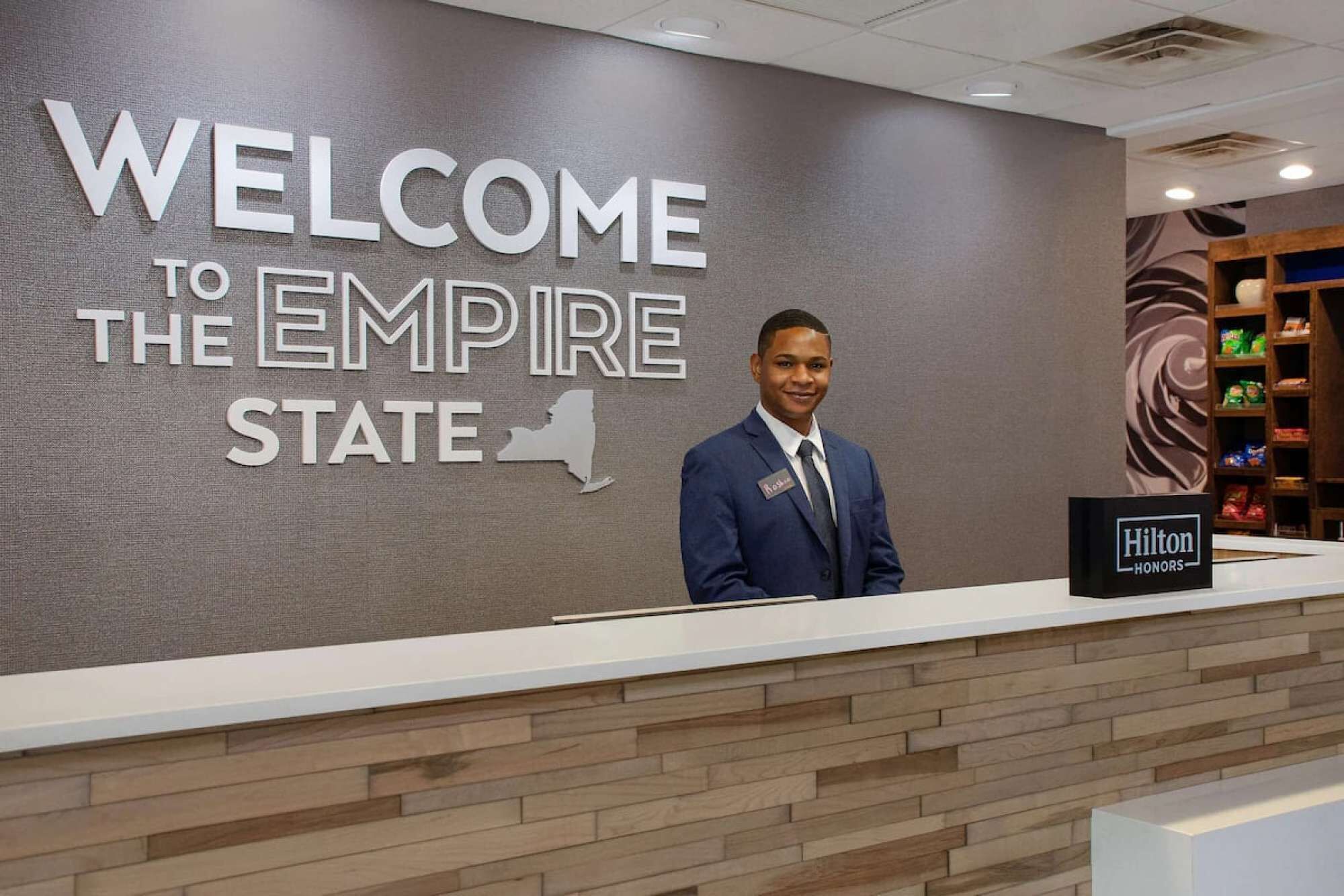 Un comptoir d’accueil d’hôtel avec une pancarte indiquant « BIENVENUE À L’EMPIRE STATE » et une autre pancarte « Hilton Honors ».