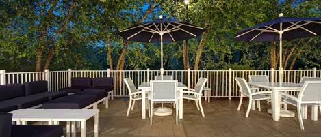 Une terrasse extérieure meublée de mobilier blanc, comprenant des canapés et des tables, et agrémentée de deux parasols pour créer de l’ombre.