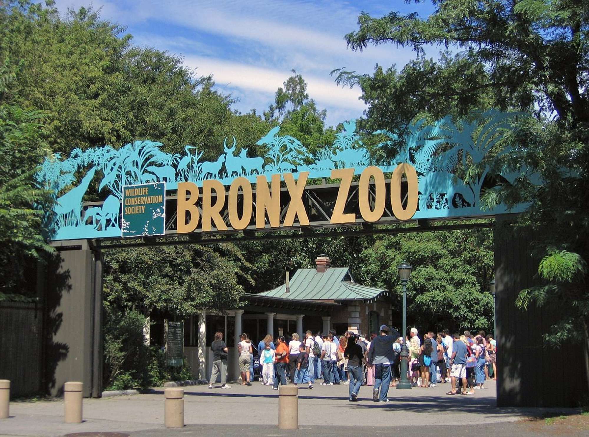 The entrance to the Bronx Zoo with a large sign and a crowd of visitors.