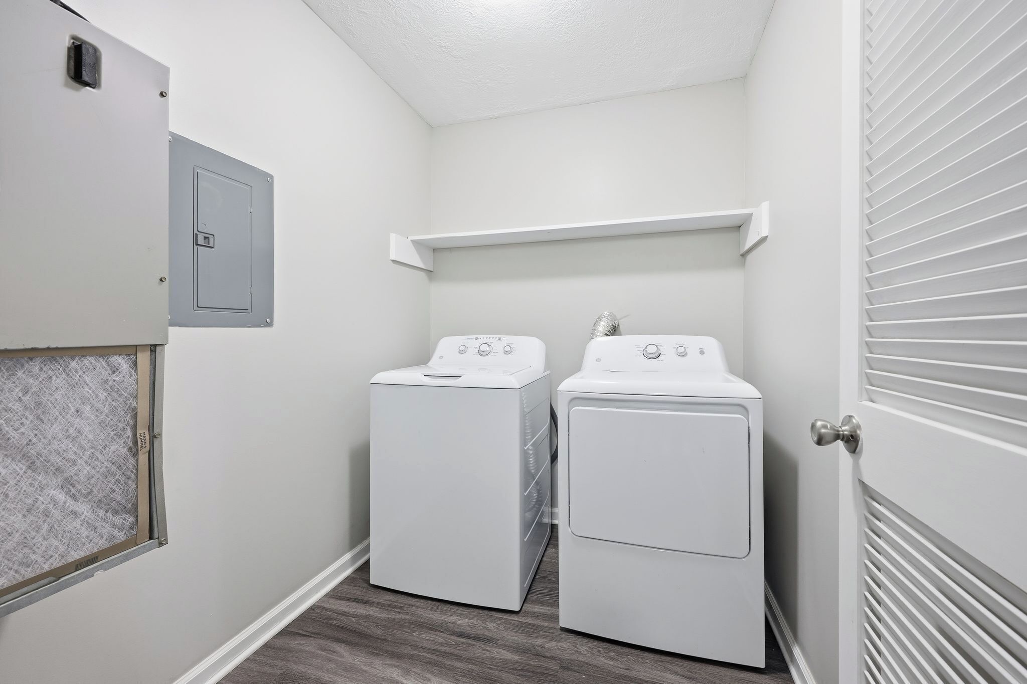 A laundry room with two white front-loading washing machines, a utility meter, and a vented dryer.