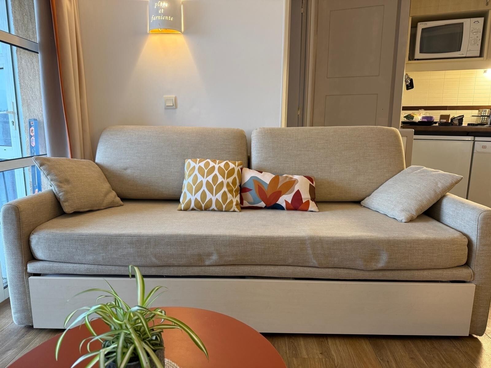 A sofa with a light-colored cushion, a patterned pillow, and a plain pillow.