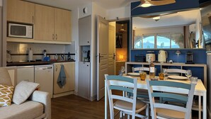 Cozinha moderna com armários de madeira, micro-ondas e área de jantar com mesa posta para dois.