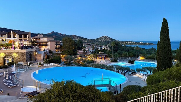 Um resort com uma piscina grande, vários edifícios e vista para o mar.