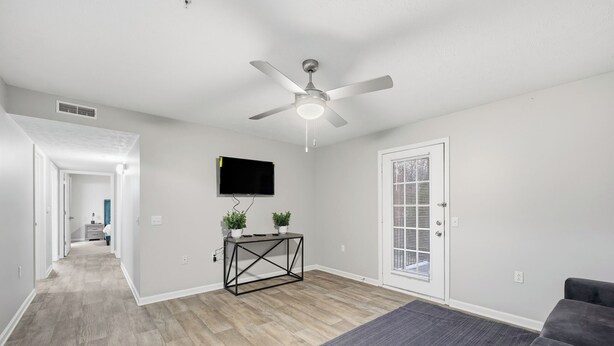 A modern living room with a ceiling fan, a flat-screen TV, a console table with plants, and a gray couch. - Stylish Highland Park 2BR 2BA Stay (Clarksville)