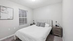 A bedroom with a bed, nightstands, a window with blinds, and a ceiling light. - Stylish Highland Park 2BR 2BA Stay (Clarksville)